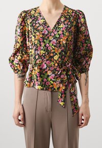Blusa con stampa floreale caratterizzata da un profondo scollo a V, maniche puff e vita legata. Il tessuto ha un aspetto texturizzato e sgualcito con colori vivaci.