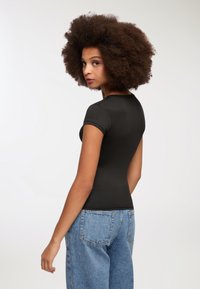 Top aderente nero a maniche corte abbinato a jeans in denim azzurro chiaro a vita alta, con una texture liscia e un design semplice.