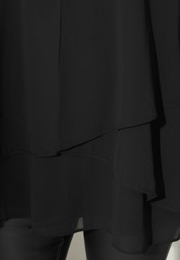 Svart lagererad topp i flödande, lätt tyg. Har ojämnt fåll och subtila sömdetaljer. Kombinerad med svarta byxor.