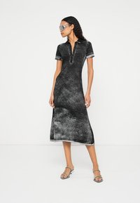 Rochie midi tie-dye neagră și gri, cu mâneci scurte și guler polo. Prezintă o croială conică și o tiv drept, purtată cu sandale cu barete.