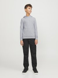 Felpa grigia chiara con tasca frontale e cappuccio, abbinata a pantaloni cargo neri con tasche laterali e sneakers nere con suola bianca.
