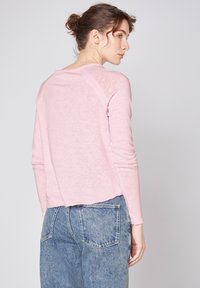 Helles rosa Langarmhemd mit abgerundetem Saum und Raglanärmeln, aus einem weichen, strukturierten Stoff. Kombiniert mit hochgeschnittenen Jeans.