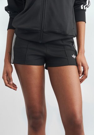 Άτομο που φοράει μαύρο αθλητικό σορτσάκι με λευκές ρίγες και μαύρο ζακέτα με φερμουάρ που ταιριάζει, με λευκές ρίγες στα μανίκια.