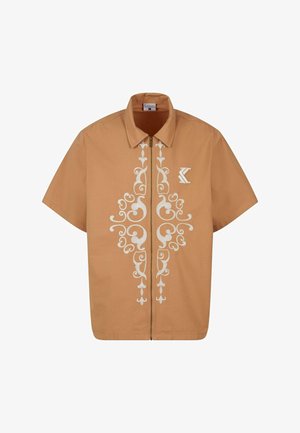 Krátky rukáv, zapínacie tričko z svetlohnedého materiálu s bielou ozdobnou kvetinovou výšivkou a logom na hrudi.