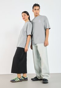 Grå bomulls t-skjorter, en med lilla logo, kombinert med et svart denimskjørt og lyseblå vide jeans. Sneakers har sorte og neongrønn detaljer.