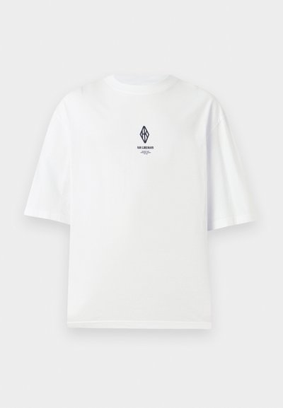 Άσπρο κοντομάνικο μπλουζάκι με μικρό μαύρο γεωμετρικό λογότυπο και κείμενο "Han Kjøbenhavn" στο κέντρο του στήθους πάνω σε απλό φόντο.