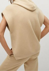 Beige ärmelloses Kapuzenshirt mit lockerer Passform, aus weichem Material gefertigt. Verfügt über weite Armausschnitte und eine glatte Textur, geeignet für lässige Kleidung.