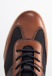 Brown leather and navy textile sneaker featuring a rounded toe, contrasting laces, and a textured finish on the upper. Rubber sole.