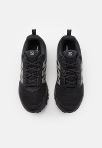 Černé sportovní boty vyrobené z prodyšného materiálu, s vyztuženou špičkou a strukturovanou podrážkou. Obsahují reflexní detaily a ploché tkaničky pro bezpečné obutí.