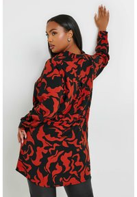 Camicia a maniche lunghe a motivo astratto in nero e rosso, con vestibilità ampia, dettagli con bottoni sulle maniche e orlo curvo.