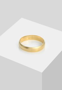 Kuldne metallist sõrmus, millel on sile ja ümar disain. Poleeritud viimistlus ja ühtlane laius, paigutatud helehalli pinna peale. Sisse on graveeritud detailid.