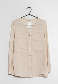 Beige skjorta med knappar i lätt tyg, med två bröstfickor, långa ärmar och rundad nederkant med knappärmar.