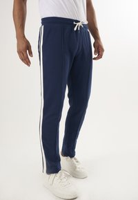 Marina sweatpants med vita sidovolanger, tillverkade av mjukt tyg. Har elastisk midja med dragsko och tapered ben-design.