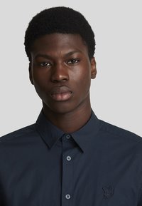 Camicia blu navy con colletto button-down, dotata di un logo ricamato discreto sul petto e in un tessuto liscio e strutturato.