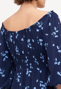 Marinekjole med lyseblå blomsterdesign, av-ellers-skulder design, smocked bodice og store ermer. Glatt stoff med delikat tekstur.