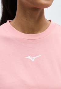 Γυναίκα που φοράει ένα ανοιχτό ροζ μπλουζάκι με στρογγυλή λαιμόκοψη και μικρό λευκό λογότυπο Mizuno στο κέντρο του στήθους.