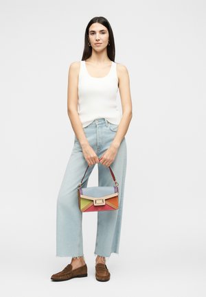 Naine pikkade tume juustega, kes kannab valget varrukateta topi, helesiniseid laia säärega teksapükse, pruune mokasiine ja hoiab värvilist geomeetrilist käekotti.