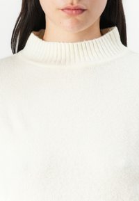 Weißer Rollkragenpullover mit einem gerippten Kragen, hergestellt aus weichem Stoff. Die Textur wirkt gemütlich und leicht flauschig. Einfaches und neutrales Design.