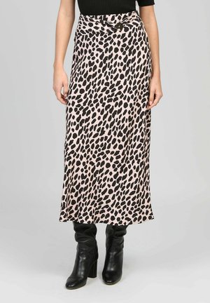 Femme portant une jupe midi rose à pois noirs avec une ceinture boutonnée, associée à des bottes en cuir noires à talons.