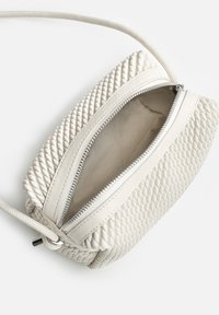 Bolso de cuero trenzado blanco bandolera con cierre de cremallera, que cuenta con un interior suave y una correa ajustable para diferentes longitudes.