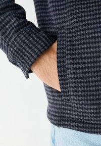 Dunkelblaues Wollhemd mit strukturiertem Karomuster, Knopfmanschette und Seitentasche; bietet eine weiche, warme Haptik und eine taillierte Passform.