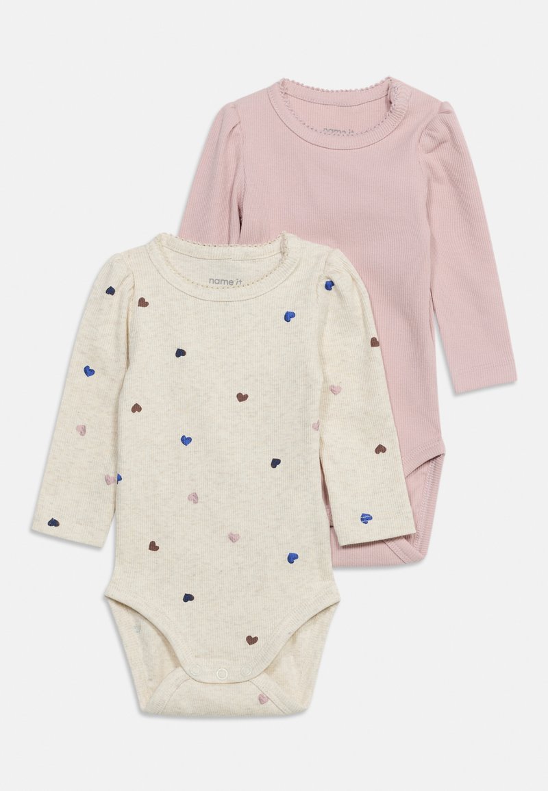Deux bodies bébé à manches longues ; un rose uni, un crème avec de petits motifs de cœurs multicolores, tous deux avec des pressions en bas.