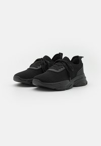 Baskets de sport noires avec une tige en maille, une pointure ronde, des lacets plats, une semelle rembourrée et un design texturé. Pas de marque visible.