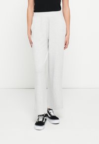 Jasnoszare dresy o luźnym kroju, z elastyczną talią i gładką fakturą, zestawione z czarnymi sneakersami z białymi akcentami.