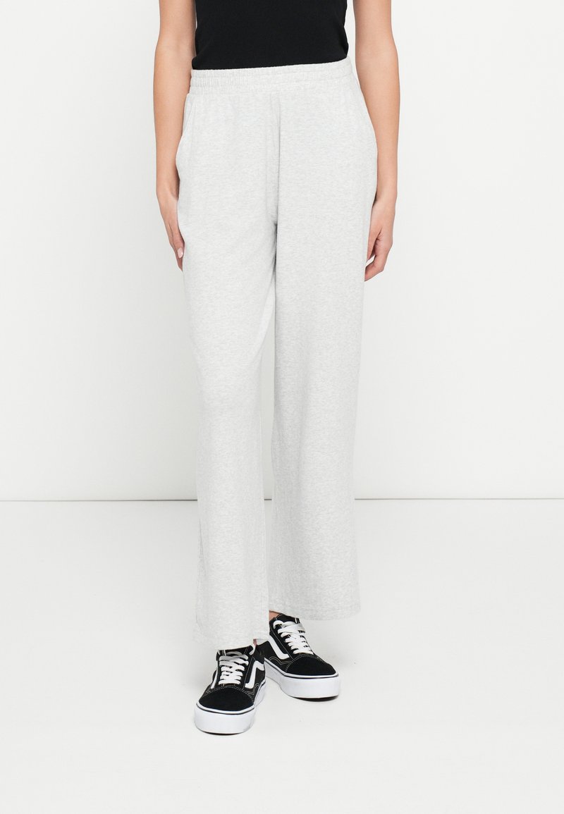 Jasnoszare dresy o luźnym kroju, z elastyczną talią i gładką fakturą, zestawione z czarnymi sneakersami z białymi akcentami.