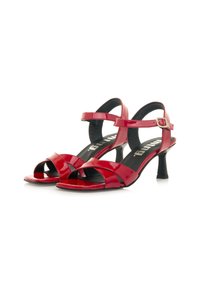 Sandalias de tacón alto de charol rojo con tiras cruzadas, hebilla en el tobillo y un tacón estrecho. Forro interior negro con branding visible.