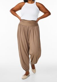 Jasnobrązowe spodnie haremowe z szerokim, elastycznym paskiem w talii, marszczonymi mankietami i luźnym krojem, w połączeniu z białym topem na ramiączkach i baletkami.
