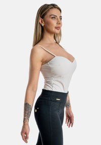 Top bianco aderente con scollatura a V e spalline sottili abbinato a leggings neri a vita alta con cuciture a contrasto e dettaglio del logo.