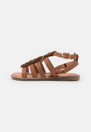 Brun læder sandal med et design med remme, flad sål, justerbar spænde og dekorative frynser på overdelen.