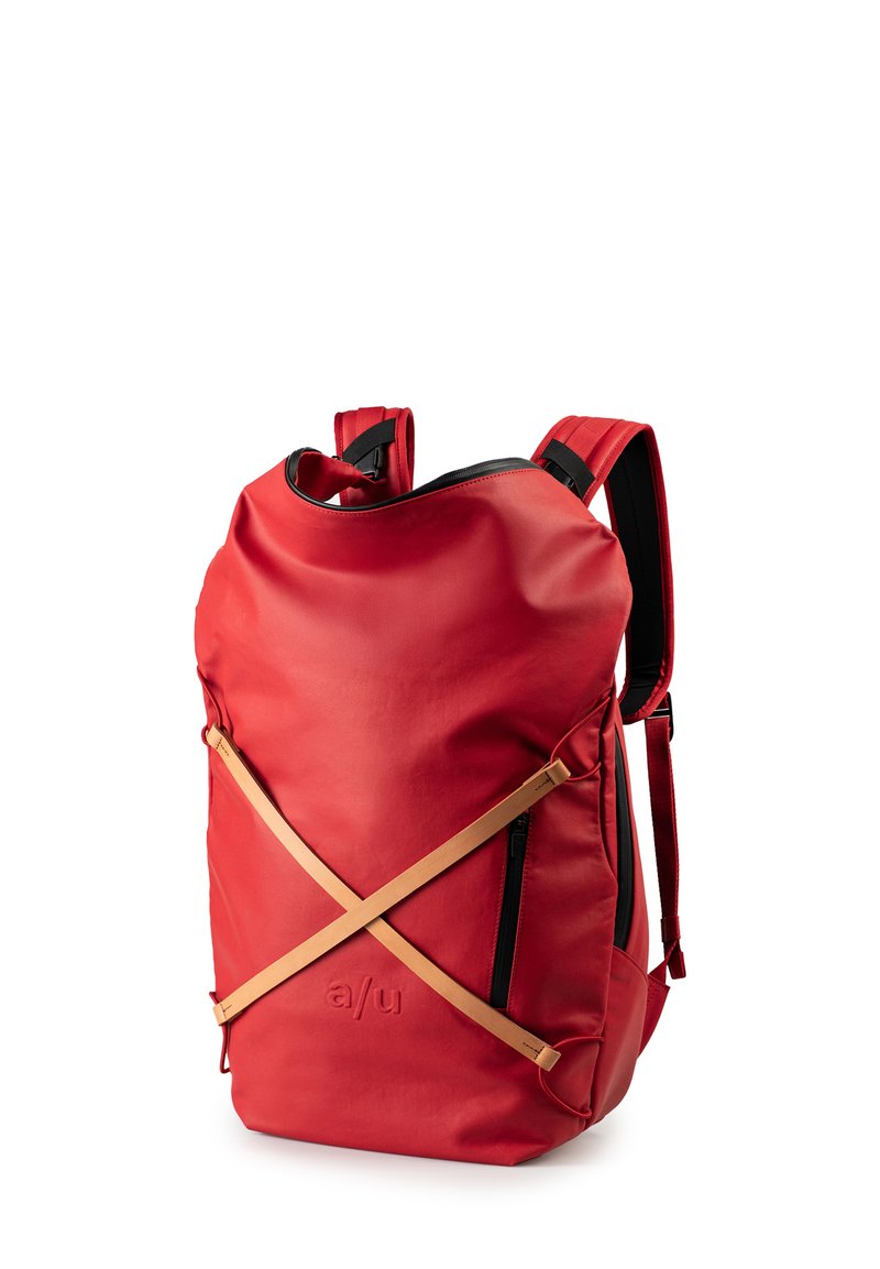 Zaino impermeabile rosso con forma arrotondata, cerniera nera e spallacci beige in contrasto disposti a forma di X sulla parte anteriore.