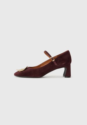 Burgundy suede heeled shoe with a pointed toe, secured by a slim strap, featuring a decorative metallic accent on the front.