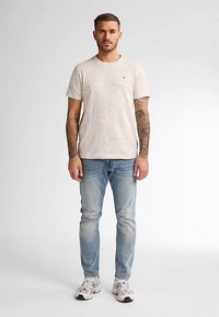 Hellbeiges meliertes T-Shirt mit kurzen Ärmeln, kombiniert mit verwaschenen blauen Jeans und weißen Sneakers. Verfügt über ein kleines Markenlogo auf der Brust.