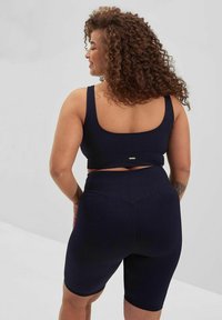 Marinblå, ribbete sports-bh og matchende høyhåndede shorts med en glatt tekstur og minimalistisk design med en liten logo-etikett.