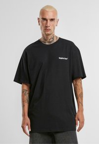 Juodas didelis t-shirt, pagamintas iš medvilnės, su trumpomis rankovėmis ir balta "pamirštų veidų" logo, atspausta ant krūtinės.