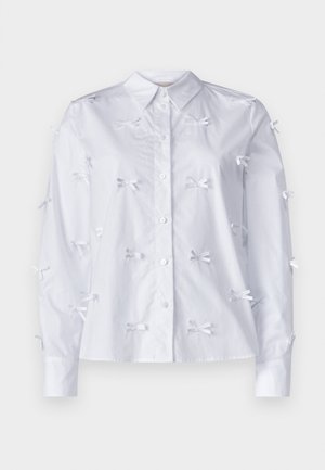 Camicia bianca a maniche lunghe realizzata in cotone, con piccoli fiocchi bianchi come decorazioni sul davanti e sulle maniche. Design con bottoni.