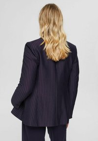 Laivaston sininen puuvillabilettä, jossa on jämäkät olkapäät, istuva leikkaus ja hienovarainen tekstuuri. Takaa katsottuna korostuu tyylikäs muotoilu.