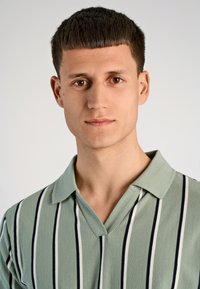 Κοντομάνικο πουκάμισο με γιακά σε ανοιχτό πράσινο χρώμα, με κατακόρυφες ναυτικές και λευκές ρίγες. Μαλακό ύφασμα με λεία υφή και κλασική γραμμή.