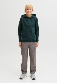 Sudadera verde con capucha y bolsillo canguro, con texto "ORIGINALS". Combinada con pantalones cargo grises, que presentan múltiples bolsillos y tobillos ajustados.