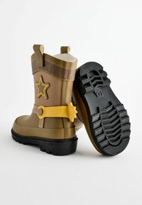 Bottes en caoutchouc de couleur marron et jaune, avec un motif d'étoile, une semelle noire texturée et des accents beiges en haut et sur la boucle.