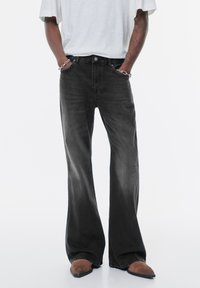 Jeans neri a gamba larga realizzati in denim con una finitura sbiadita. Presentano una chiusura con bottone e cerniera, tasche frontali e una vestibilità casual.