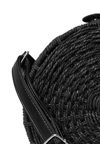 Borsa circolare intrecciata nera con un aspetto testurizzato, dotata di una tracolla in pelle nera liscia e accessori metallici.