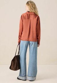 Satin rust blouse with a back yoke, paired with light blue flared denim, and a brown leopard-print tote bag, featuring a flat handle.