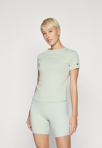 Lys grønn treningstopp med korte ermer og tettsittende shorts, laget av glatt, elastisk materiale, med en tonet design og logodetalj.