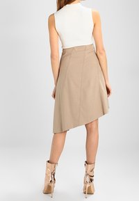Jupe beige en A avec un ourlet asymétrique, associée à un haut blanc ajusté en maille côtelée et des bottines métalliques en rose gold.