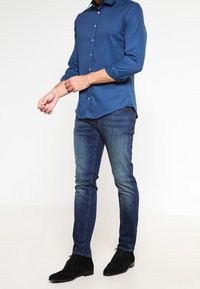 Blauw shirt met lange mouwen, getailleerd ontwerp, knoopsluiting aan de voorkant, gecombineerd met donker denim jeans en zwarte suède schoenen. Simpele, klassieke stijl.