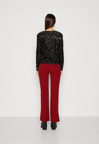 Svart paljett-top med långa ärmar, kombinerad med högmidjade bordeauxfärgade byxor. Outfiten har en figurnära silhuett och svarta klackskor med blockklack.